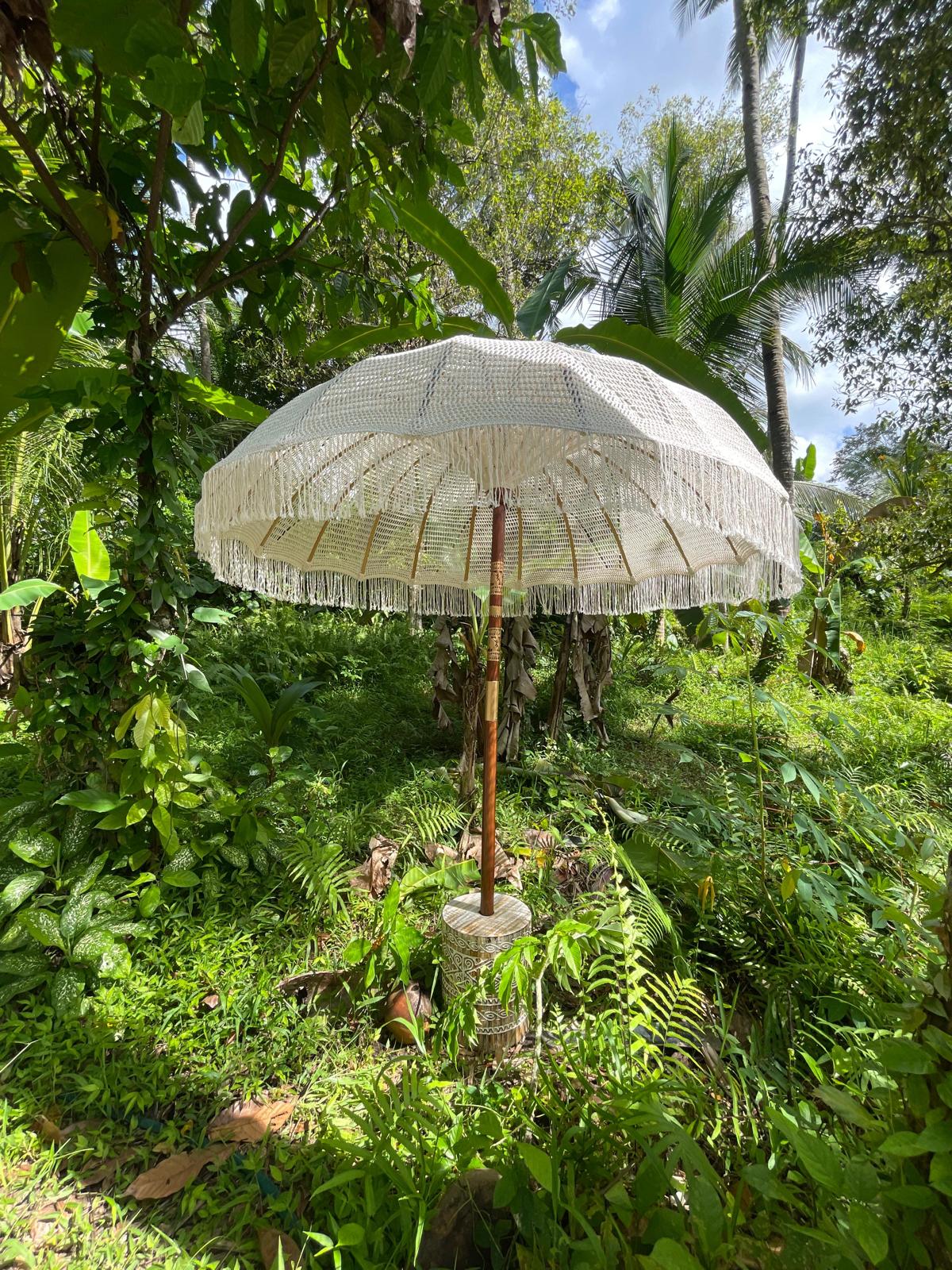 Gustae Oriental cream Bali umbrella standing in a Balinese garden, banana plants and ferns behind